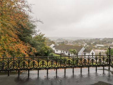 A view from a balcony with a decorative iron railing overlooking houses trees and a town in the distance at Holcombe House in Torquay