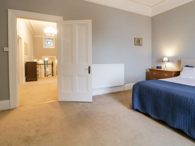 A bedroom with a blue bedspread a wooden nightstand with a lamp digital clock and an open door showing a hallway at Holcombe House in Torquay