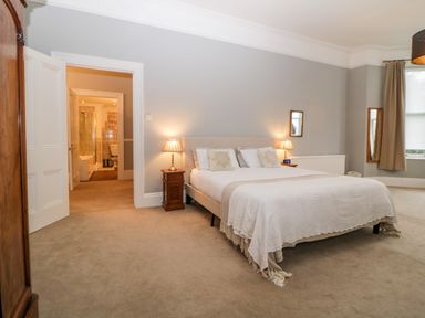 A bedroom with a double bed two bedside tables with lamps an open door leading to a bathroom and a window with curtains at Holcombe House in Torquay