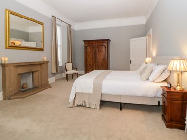 A bedroom with a bed side tables lamps a chair wardrobe fireplace and a mirror at Holcombe House in Torquay