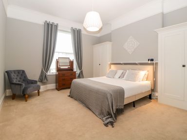 A bedroom with a bed a gray chair a wooden dresser and two white wardrobes at Holcombe House in Torquay