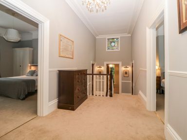 A hallway with a wooden chest of drawers and a stained glass window with rooms visible at Holcombe House in Torquay