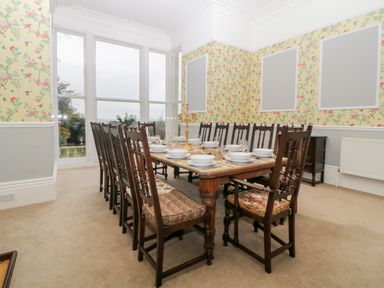A dining room with a long wooden table set with plates and glasses and wooden chairs around Holcombe House in Torquay