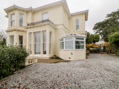 Exterior view of a two story house with large windows and a conservatory with gravel driveway and outdoor seating area at Holcombe House in Torquay