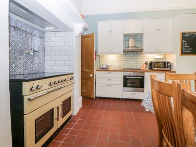 A kitchen with a large stove, white cabinets, wooden door, and wooden chairs at Holcombe House in Torquay