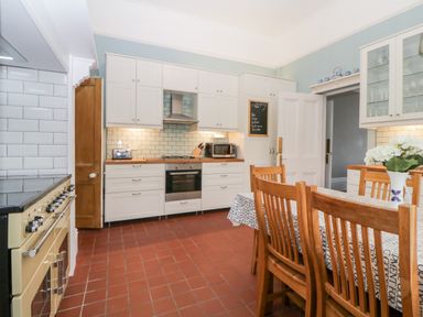 A kitchen with white cabinets a wooden dining table and chairs and a cooking range at Holcombe House in Torquay