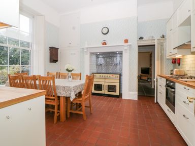 A kitchen with a wooden dining table and chairs a large window and a stove at Holcombe House in Torquay