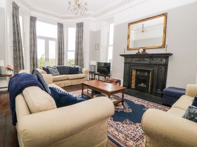 A living room with beige sofas a wooden coffee table a black fireplace with a large mirror above and patterned curtains at Holcombe House in Torquay