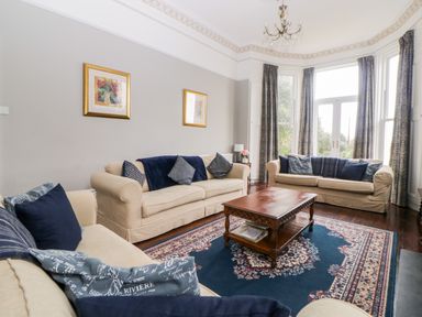 A living room with beige sofas blue cushions a wooden coffee table and large windows at Holcombe House in Torquay