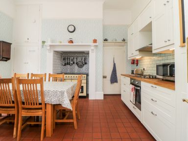 A kitchen with wooden dining table and chairs tiled floor white cabinets and cooking utensils at Holcombe House in Torquay