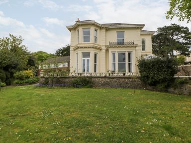 Exterior view of a two story house with large windows a stone wall and a lawn at Holcombe House in Torquay
