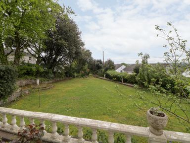 A garden with grass, trees, and bushes viewed from a white stone balustrade at Holcombe House in Torquay