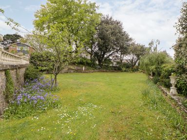 A garden with grass and flowers bordered by trees and stone walls at Holcombe House in Torquay