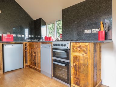 A kitchen with wooden cabinets a dishwasher a stove and red kitchen containers at The Hideout in Llangrove