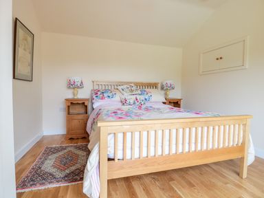 A bedroom with a wooden bed with floral bedding two bedside tables with lamps and a rug on the wooden floor at The Hideout in Llangrove