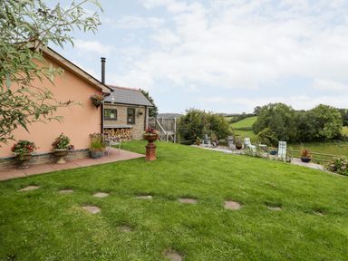 A backyard with green grass plants and patio furniture overlooking trees and fields at The Hideout in Llangrove
