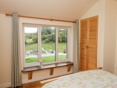 A bedroom with a window seat and wooden wardrobe overlooking a garden at The Hideout in Llangrove