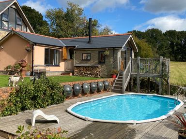 An outdoor swimming pool with a wooden deck next to a house and garden at The Hideout in Llangrove