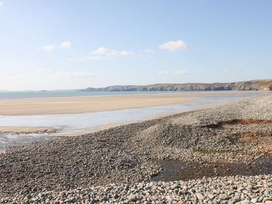 A pebble beach with sand and cliffs in the distance under a blue sky at Mill View in Neyland