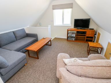 A living room with sofas a wooden coffee table a television on a wooden stand and a window at Mill View in Neyland
