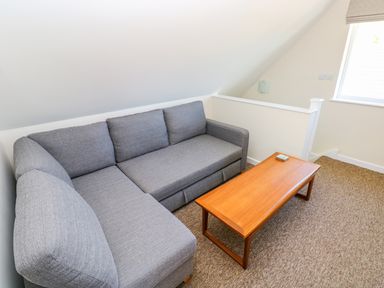 A grey sectional sofa and a wooden coffee table in a room with carpeted floor and a window at Mill View in Neyland
