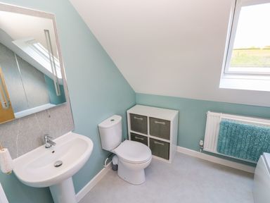 A bathroom with a sink a toilet a storage unit a window and a radiator with a blue towel at Mill View in Neyland