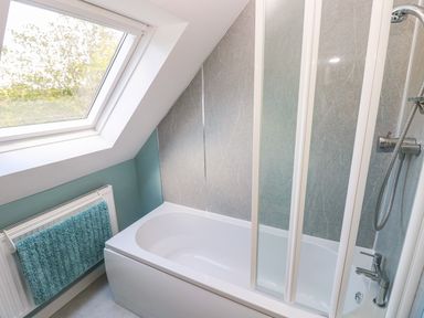 A bathroom with a bathtub shower combination a glass shower screen a towel hanging on a radiator and a window at Mill View in Neyland