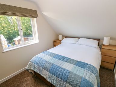 A bedroom with a double bed and blue patchwork quilt near a window with trees outside at Mill View in Neyland