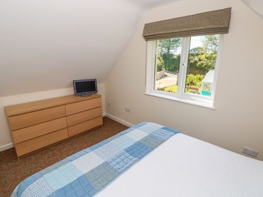 A bedroom with a bed covered with a blue patchwork quilt a wooden dresser with a small TV on top and a window with a garden view at Mill View in Neyland