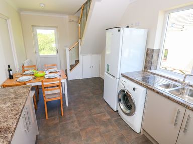 A kitchen with a dining table set for four chairs under stairs cabinets refrigerator washing machine and double sink at Mill View in Neyland