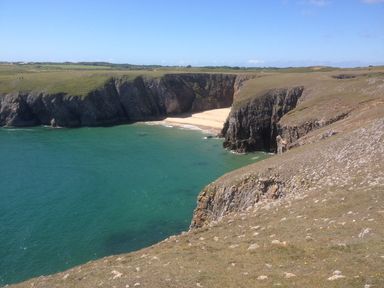 A rocky coastline with cliffs surrounding a small sandy beach and turquoise water at Mill View in Neyland