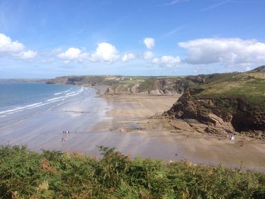 A sandy beach with people walking near cliffs and grassy hills under a blue sky at Mill View in Neyland