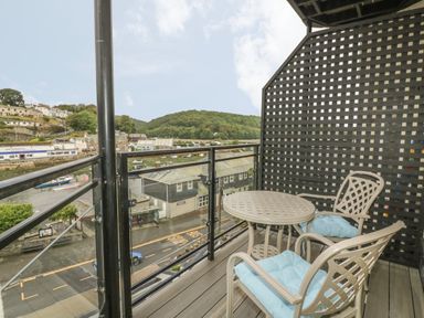 A balcony with two chairs and a round table overlooking a street and river at Harbour View Apartment in Looe