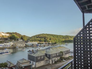 A river with boats and buildings near a forested hill at Harbour View Apartment in Looe