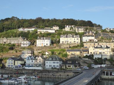 Houses on a hillside overlooking a harbor with boats and a road leading to a bridge at Harbour View Apartment in Looe