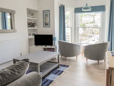 A living room with two armchairs by a large window and a television on a white stand at Harbour View Apartment in Looe