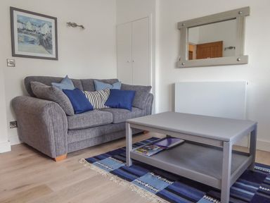 A living room with a gray sofa with blue cushions a gray coffee table on a blue striped rug and a wall mirror at Harbour View Apartment in Looe