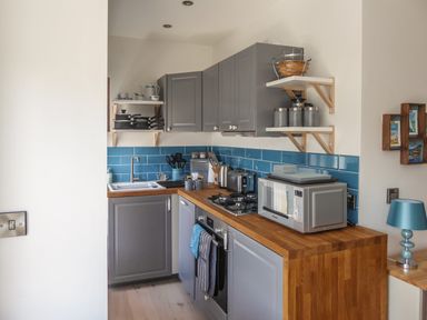 A kitchen with gray cabinets wooden countertops blue tiled backsplash and various appliances at Harbour View Apartment in Looe