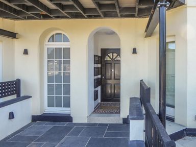 An outdoor entrance area with a black door white window tiled floor and black railings at Harbour View Apartment in Looe