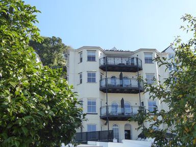 A multi-story residential building with balconies surrounded by green trees at Harbour View Apartment in Looe