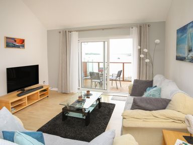 A living room with sofas cushions a glass coffee table tv and sliding doors to a balcony at Delfryd in Y Felinheli