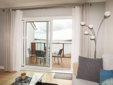 A living room with a glass coffee table and a sofa looking out to a balcony with chairs and a table by the water at Delfryd in Y Felinheli