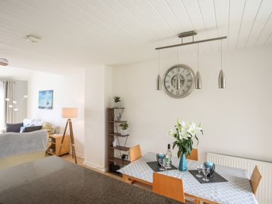A dining table with flowers and wine glasses next to a living area with sofas and a floor lamp at Delfryd in Y Felinheli