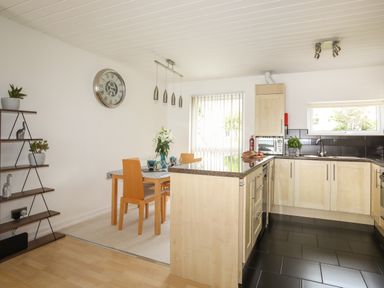 A kitchen and dining area with wooden cabinets a dining table with chairs and shelving unit with plants at Delfryd in Y Felinheli