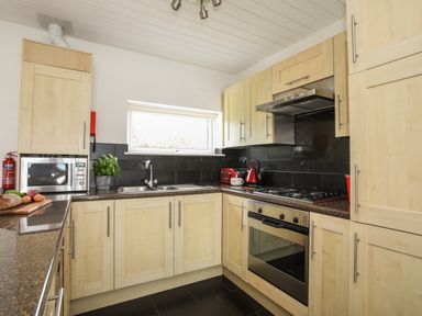 A kitchen with wooden cabinets a microwave a sink a gas stove red kettle and toaster at Delfryd in Y Felinheli
