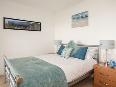 A bedroom with a metal bed frame blue and teal pillows and blanket two wooden bedside tables with lamps and alarm clock at Delfryd Y Felinheli