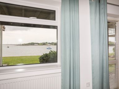 A window with blue curtains and radiator below showing a view of boats on water and greenery at Delfryd in Y Felinheli