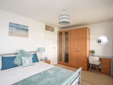 A bedroom with a bed, bedside table, wardrobe, desk with chair, and mirror at Delfryd in Y Felinheli