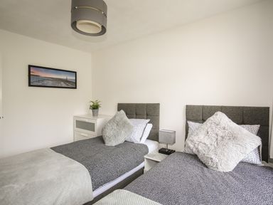 A bedroom with two single beds bedside table lamp plant on a cabinet and wall art at Delfryd in Y Felinheli