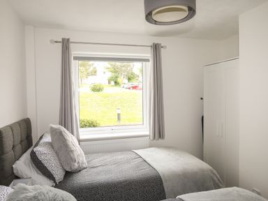 A bedroom with two single beds a window with curtains and a white wardrobe at Delfryd in Y Felinheli